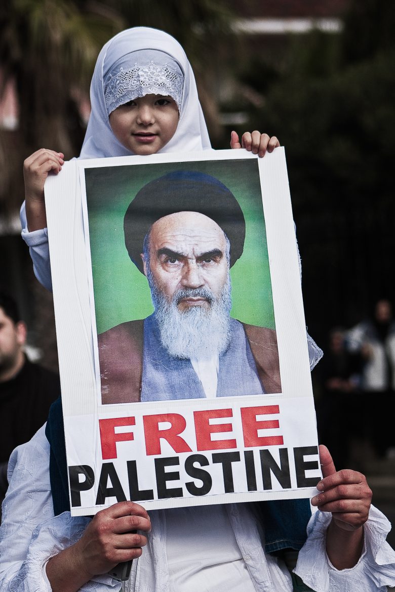 A girl sitting on his fathers shoulders hold a sign with the words "FREE Palestine".